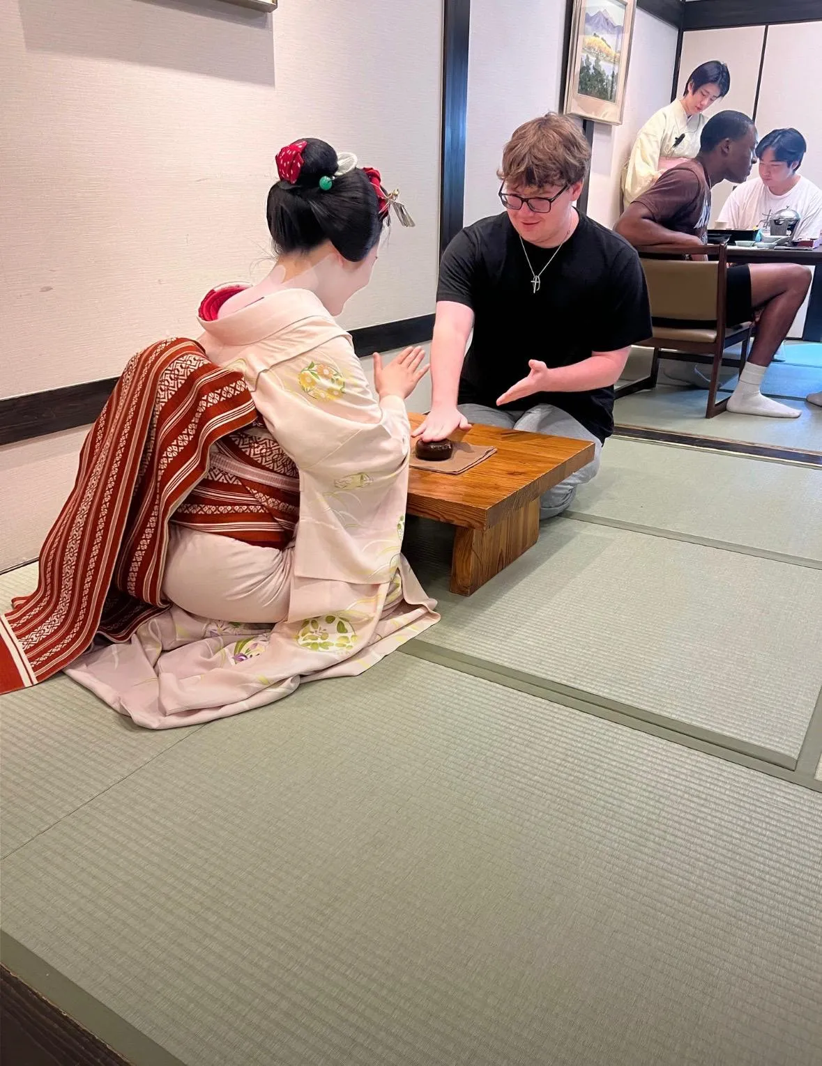 Levi at a low table with an apprentice geisha in a tatami room in Japan.