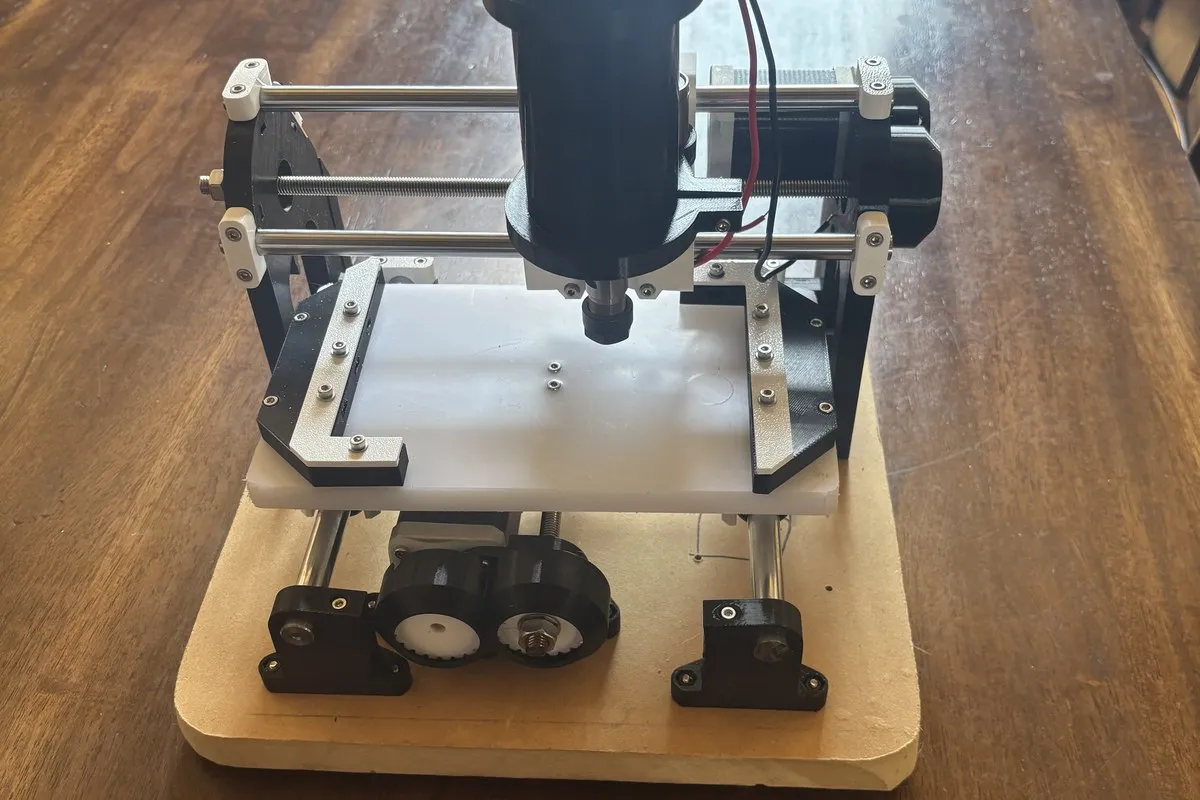 A compact CNC mill assembled on an MDF base — 3D-printed mounts, lead screws, and a spindle over the bed.