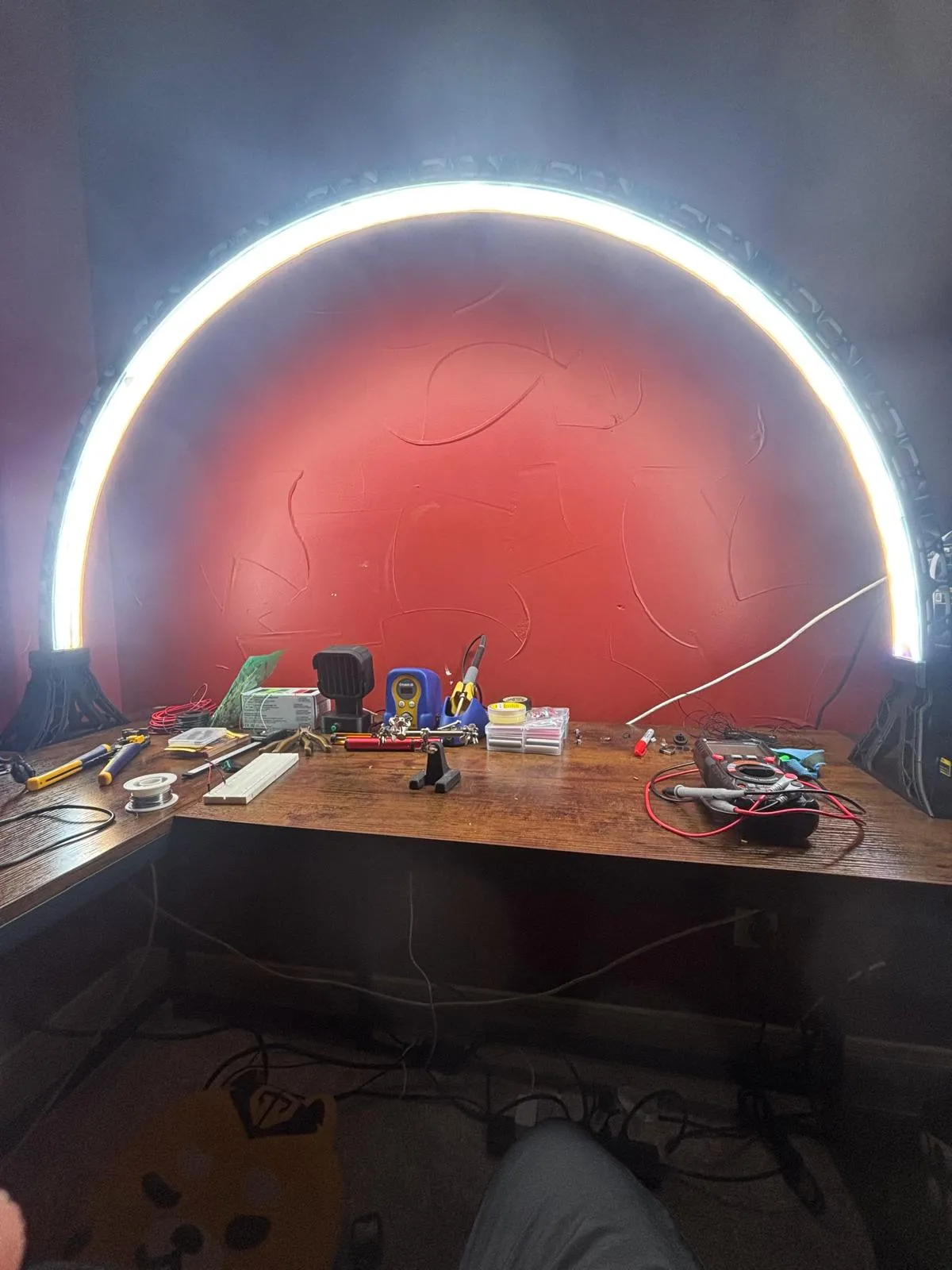 A warm-white LED arc lighting a workbench of soldering tools and electronics.