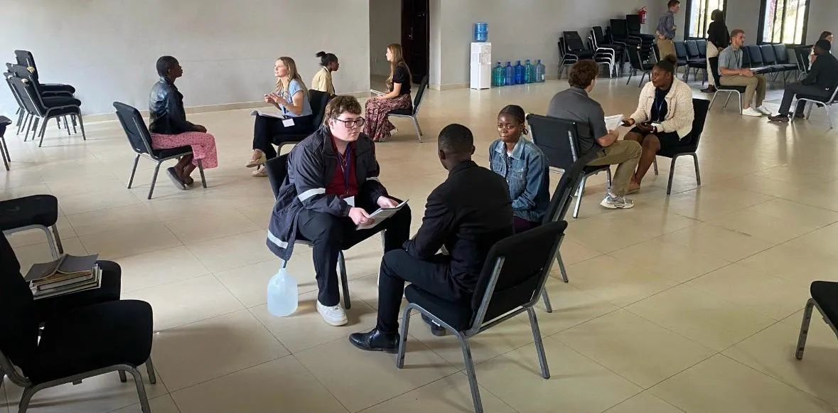 Levi talking one-on-one with a student in a hall of paired chairs.